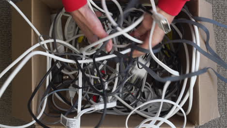 top view of hands successfully untangling one electronics cord from many in a box