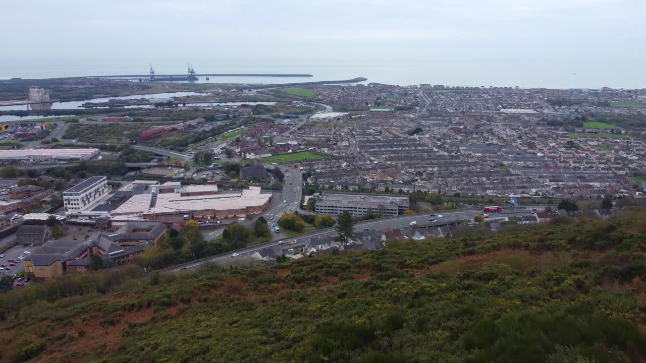 Ripresa aerea in allontanamento di Port Talbot da una collina con l'autostrada M4 trafficata e un sentiero escursionistico sopra 4K