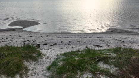 a peaceful beach scene during sunset, showcasing a small tidal pool reflecting the light on its surface, surrounded by sandy shores and patches of grass