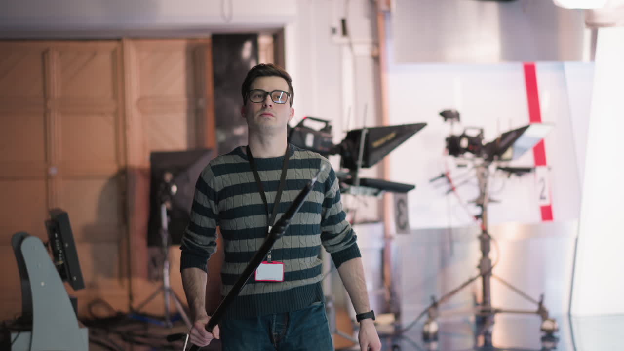 Technician in broadcast studio adjusting boom pole, preparing for filming. Focused on controlling equipment and positioning lighting in modern media production environment