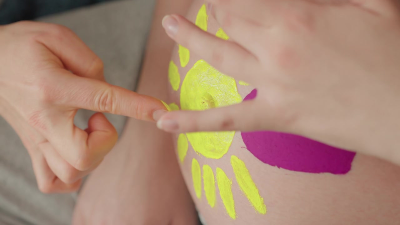 Woman Painting Sun and Heart on Pregnant Belly