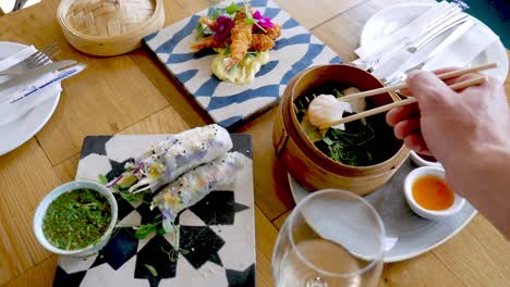person use chopsticks to dip dim sum in tangy sauce, table with asian cuisine