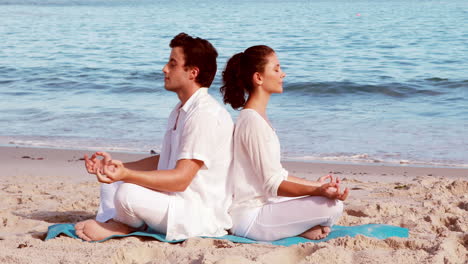 Peaceful-couple-meditating-in-lotus-pose-at-the-beach