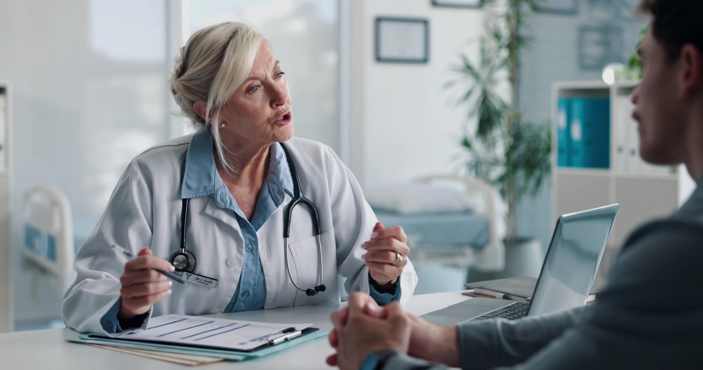 Senior Female Doctor Consulting with Male Patient in Clinic