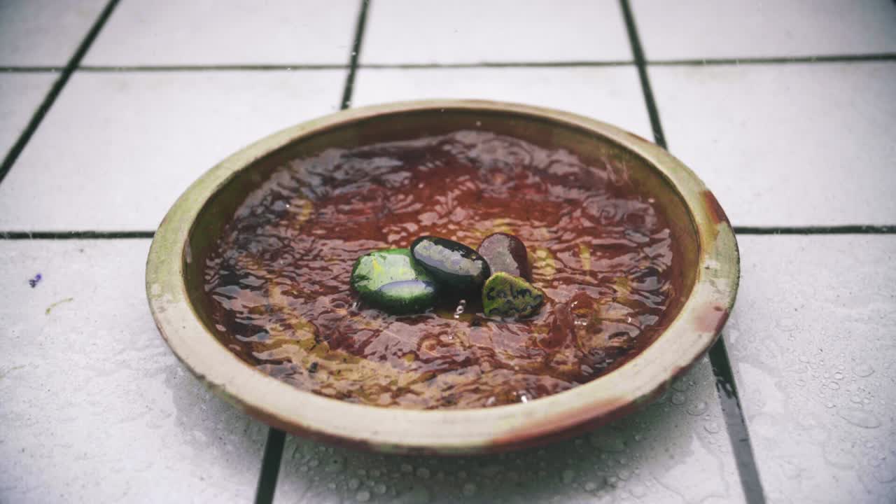 슬로우 모션 비가 표면에 잔물결을 형성하는 배경에 흰색 타일이 있는 갈색 꽃 점토 항아리를 범람시키는 클로즈업 잠금 샷