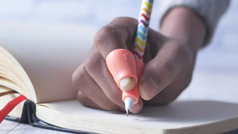 person writing in a notebook with a pen and thumb grip