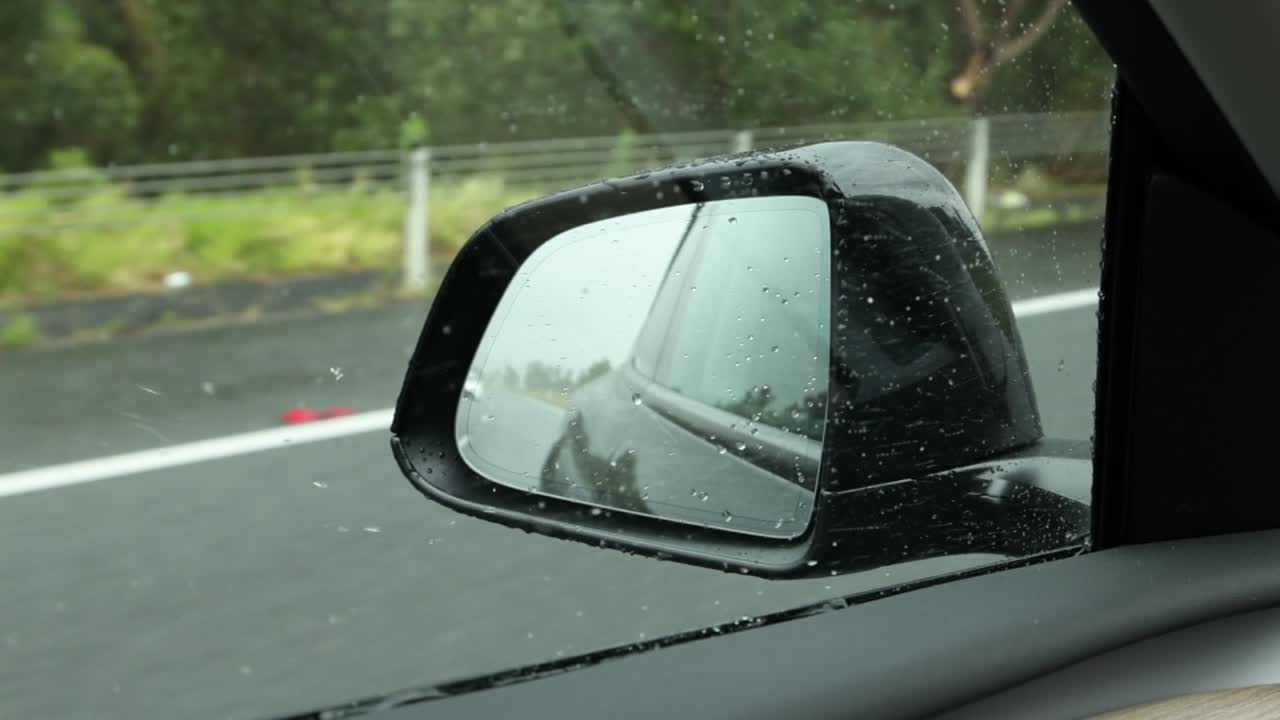 Close-up view of raindrops on a car side mirror while driving on a wet road.