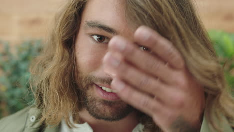 close-up-portrait-of-relaxed-young-caucasian-man-with-beard-running-hand-through-hair-smiling-happy