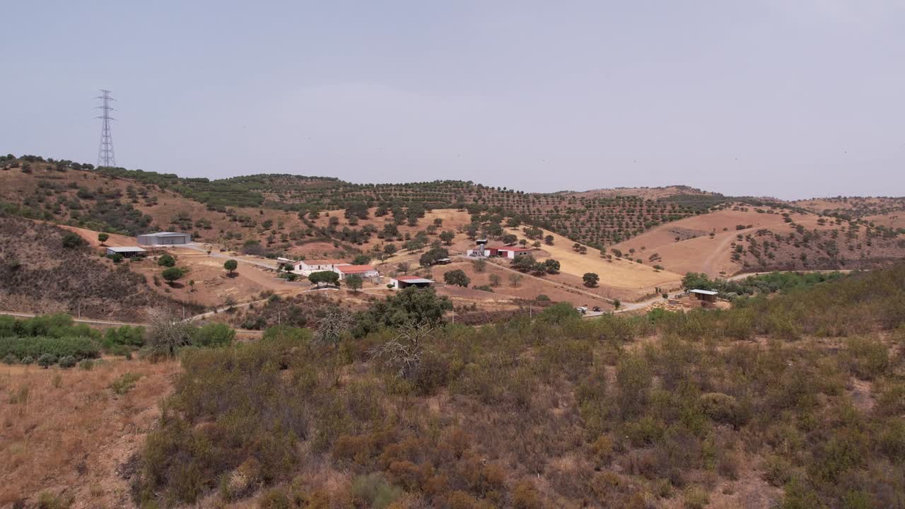 Drone che vola sopra una valle boscosa verso un magazzino agricolo in un paesaggio rurale