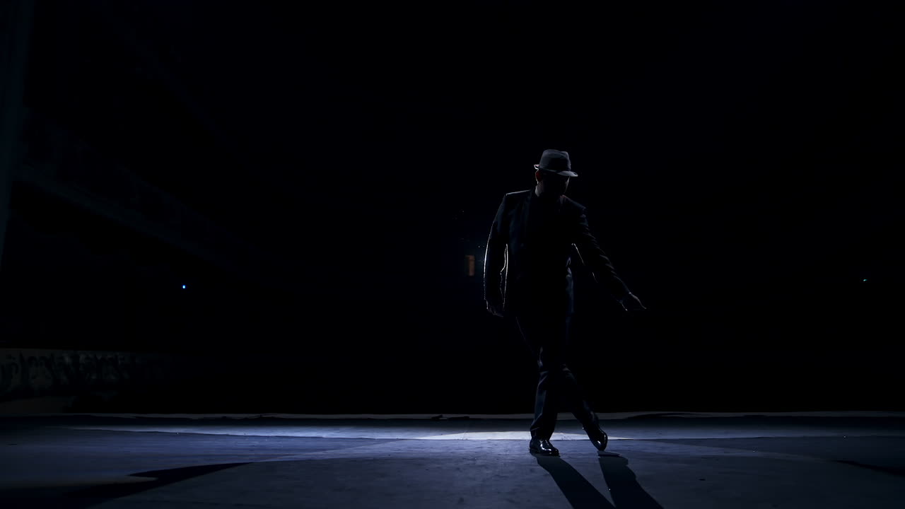 Silhouette of a man in classic hat and suit dances on a stage of classic theater. Dark light on stage. Concept video.