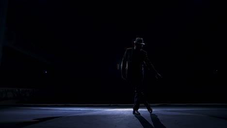 silhouette of a man in classic hat and suit dances on a stage of classic theater. dark light on stage. concept video.