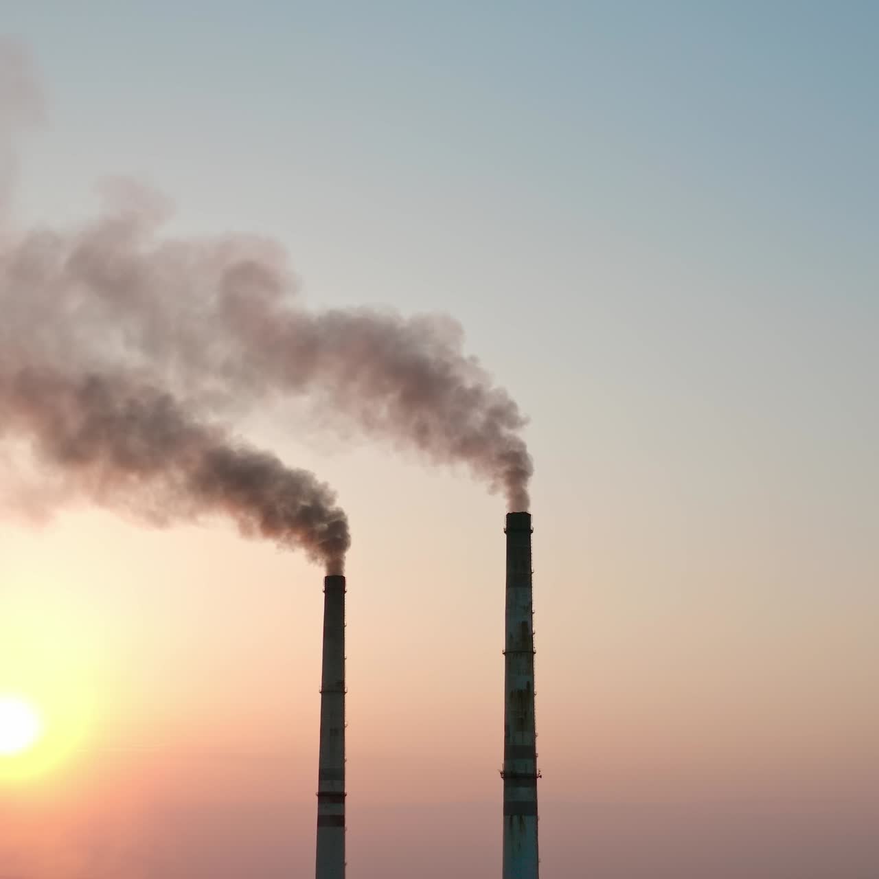 Smoke pipes on clear evening sky background. Factory chimneys release dark emissions into the atmosphere. Chemical smoke pollute the air. Ecology in danger