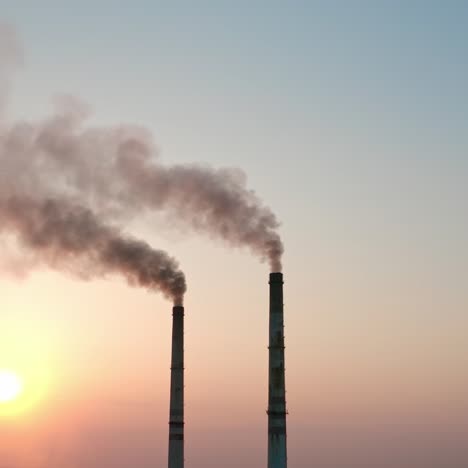 Smoke pipes on clear evening sky background. Factory chimneys release dark emissions into the atmosphere. Chemical smoke pollute the air. Ecology in danger