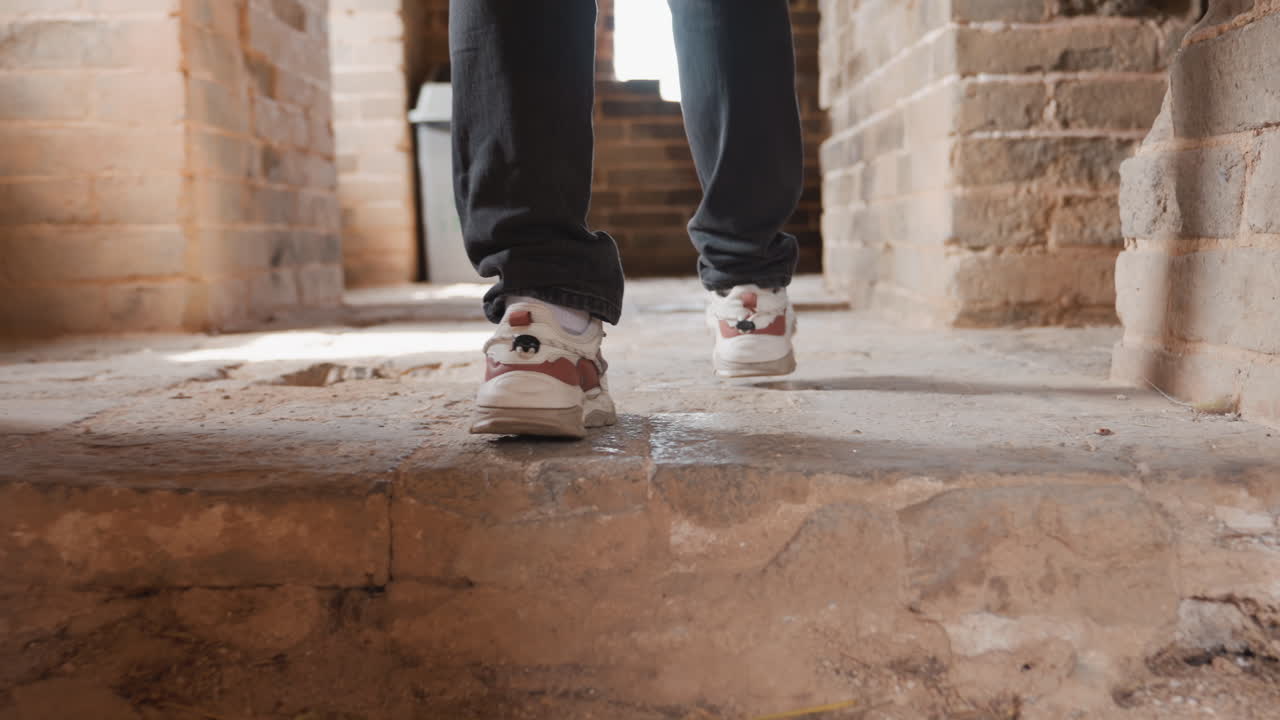 Sunlit brick corridor with steady steps person walking confidently in casual sneakers and jeans light streaming across textured floor closeup of soles and tread recycling bin visible in background