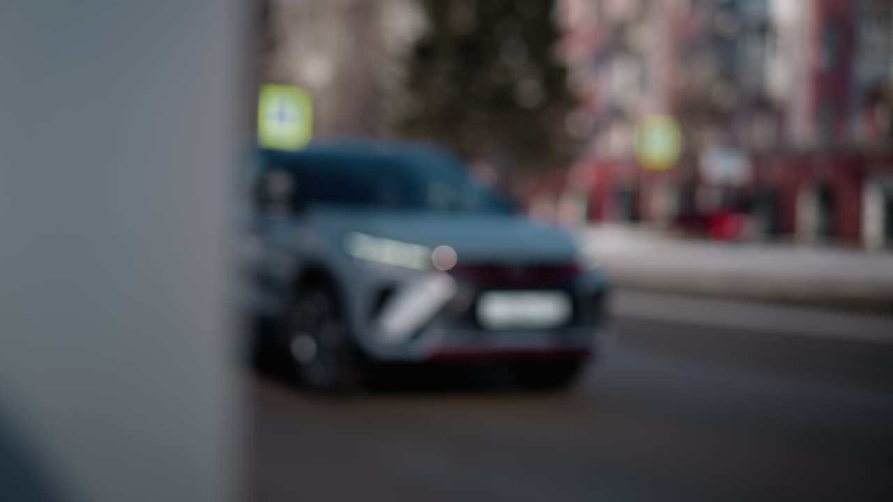 blur cars glide along city street, soft focus suv passes with headlights glowing, buildings and signs dissolve into bokeh, urban motion conveys commute mood, passing traffic, afternoon haze