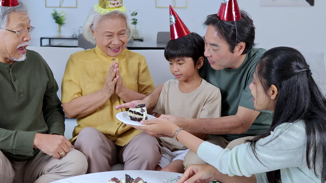 Three generations enjoy birthday cake together in a brightly lit living room, festive and joyful