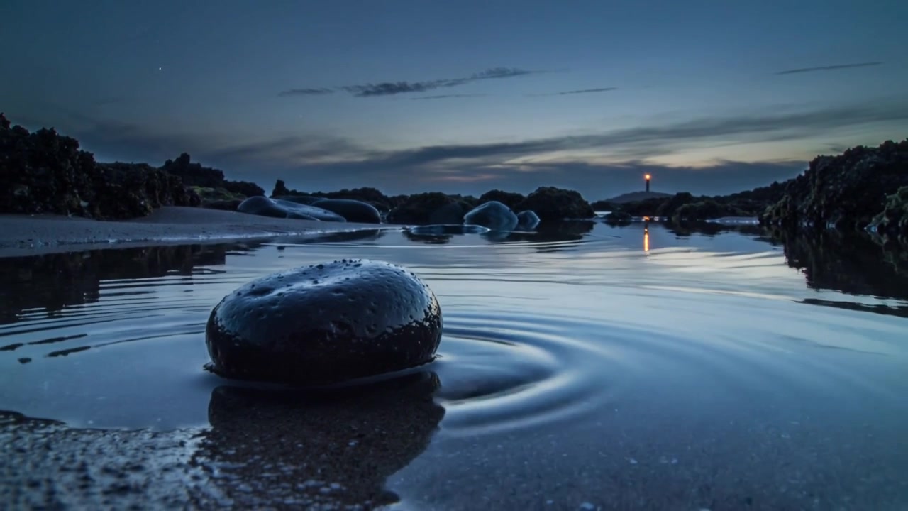 Ripples radiating from cobble in tidal pool at dusk after disturbance, with lighthouse reflection