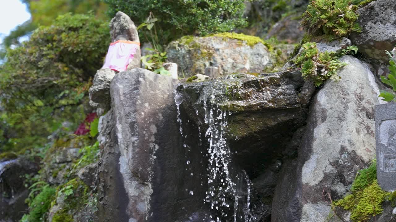 estatua de jizo de musgo y agua que fluye sobre la roca en el jardín japonés en cámara lenta