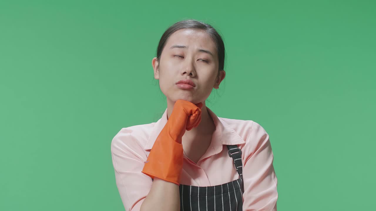 초록색 스크린 스튜디오에서 그녀의 지표손가락을 올리는 무언가에 대해 생각하고 주위를 둘러보는 아시안 여성 집주인의 클로즈업