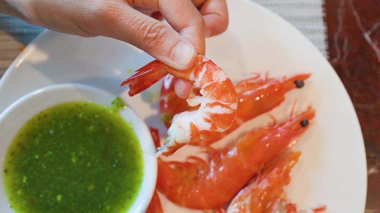 Primo piano dall'alto di mani che sbucciano gamberi bolliti, serviti con salsa piccante verde per frutti di mare.