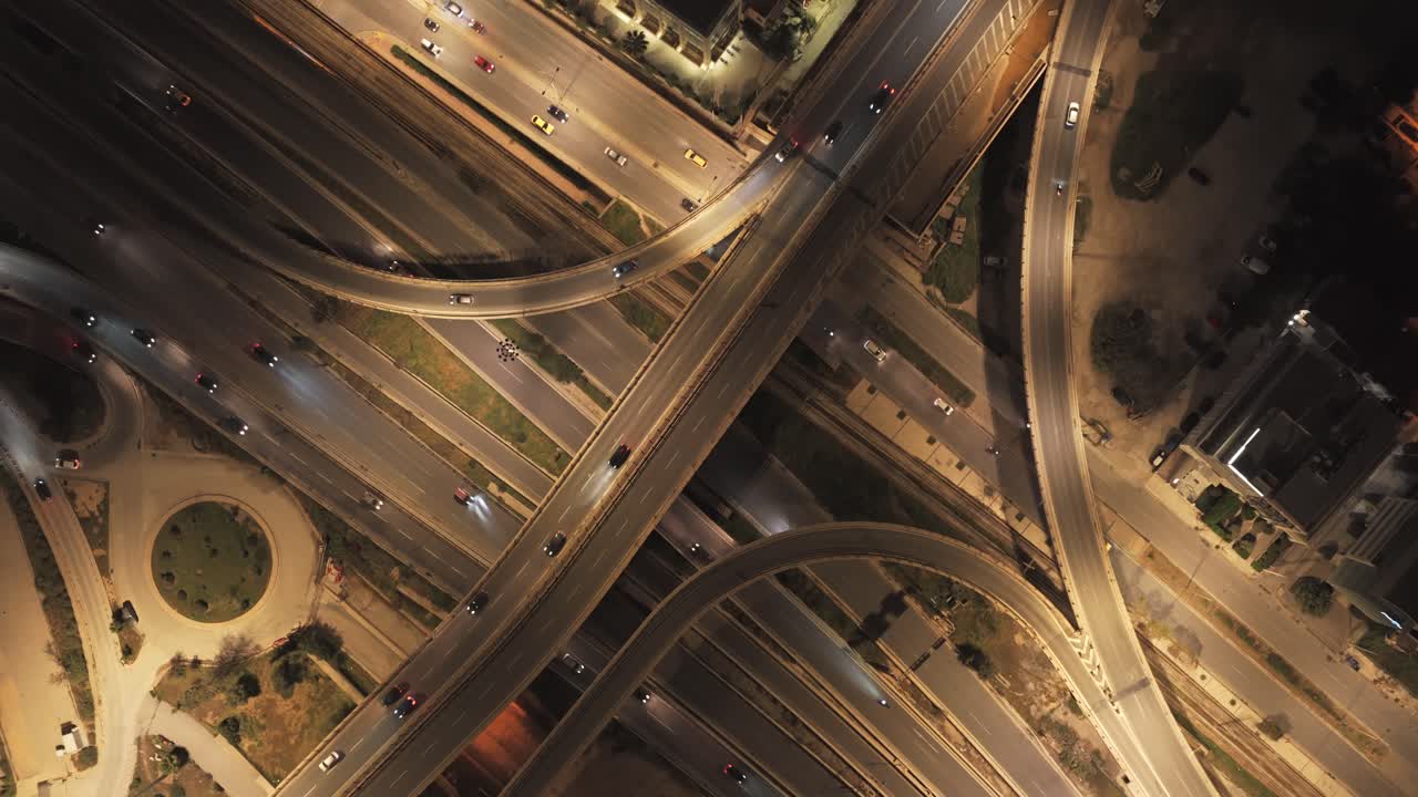 Luminous aerial view capturing the intricate network of a bustling highway interchange at night, with cars creating trails of light as they navigate the complex road system