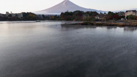 aerial view low over a misty lake, revealing a fisherman and mt fuji, fall in japan