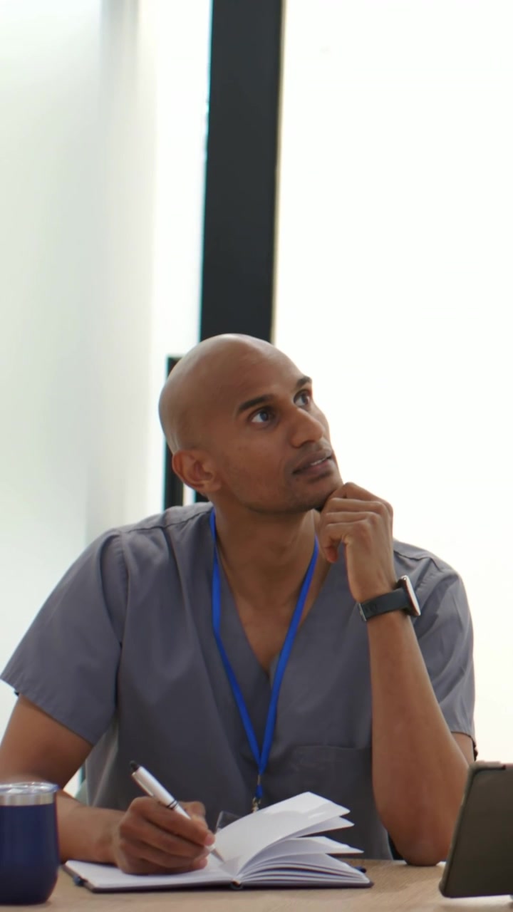 Vertical video: Taking notes doctor in scrubs with ID following meeting at table with notebook pen