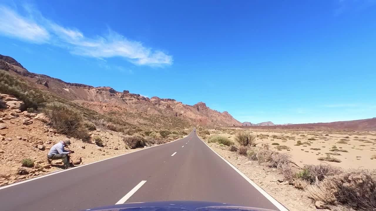 Coche azul conduciendo por una carretera recta con cielo azul y nubes blancas, paisaje desértico, punto de vista del conductor, FPV