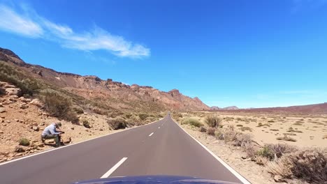 blue car driving on a straight road with blue sky and white clouds, desert landscape, driver point of view, fpv