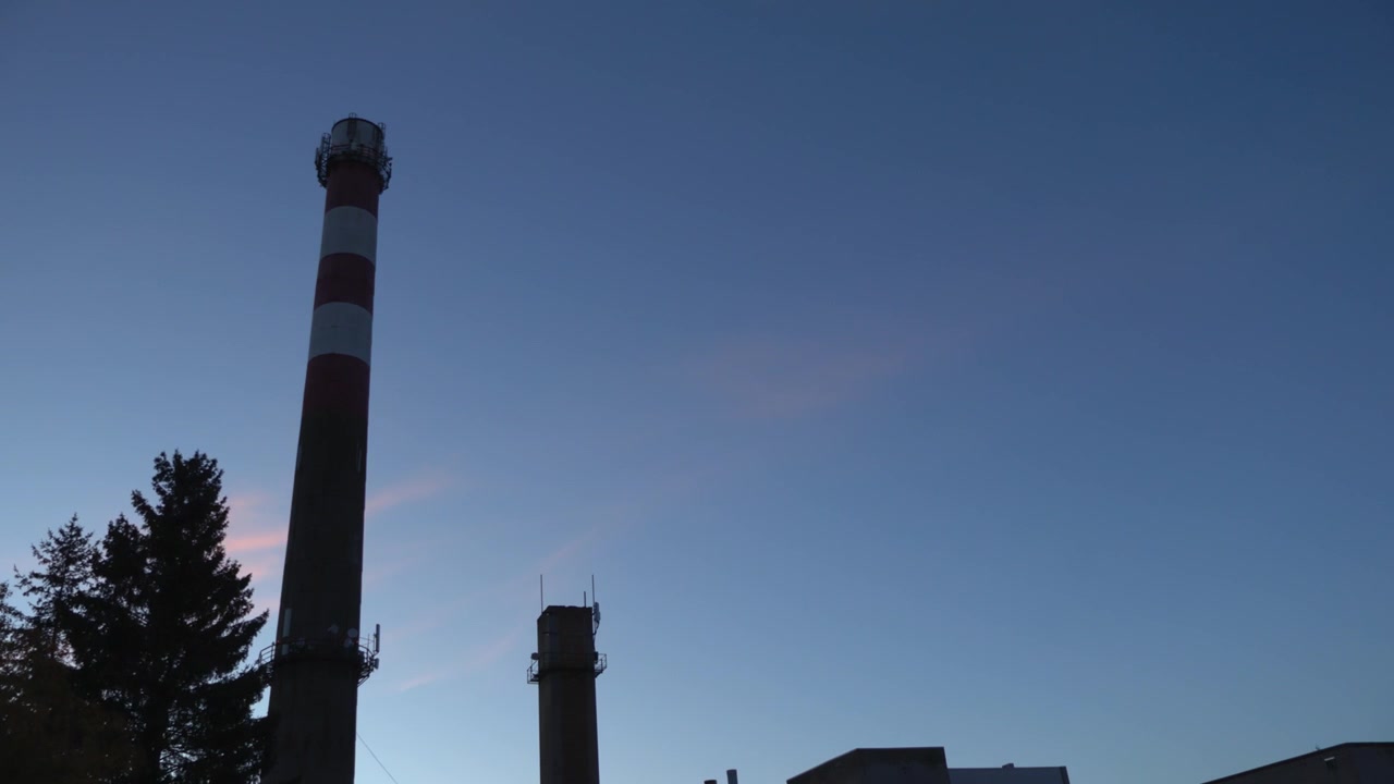 Smoke stack chimney or factory pipe time lapse or timelapse in Laagri Estonia during a sunny afternoon or evening while some clouds move in the blue sky behind it.