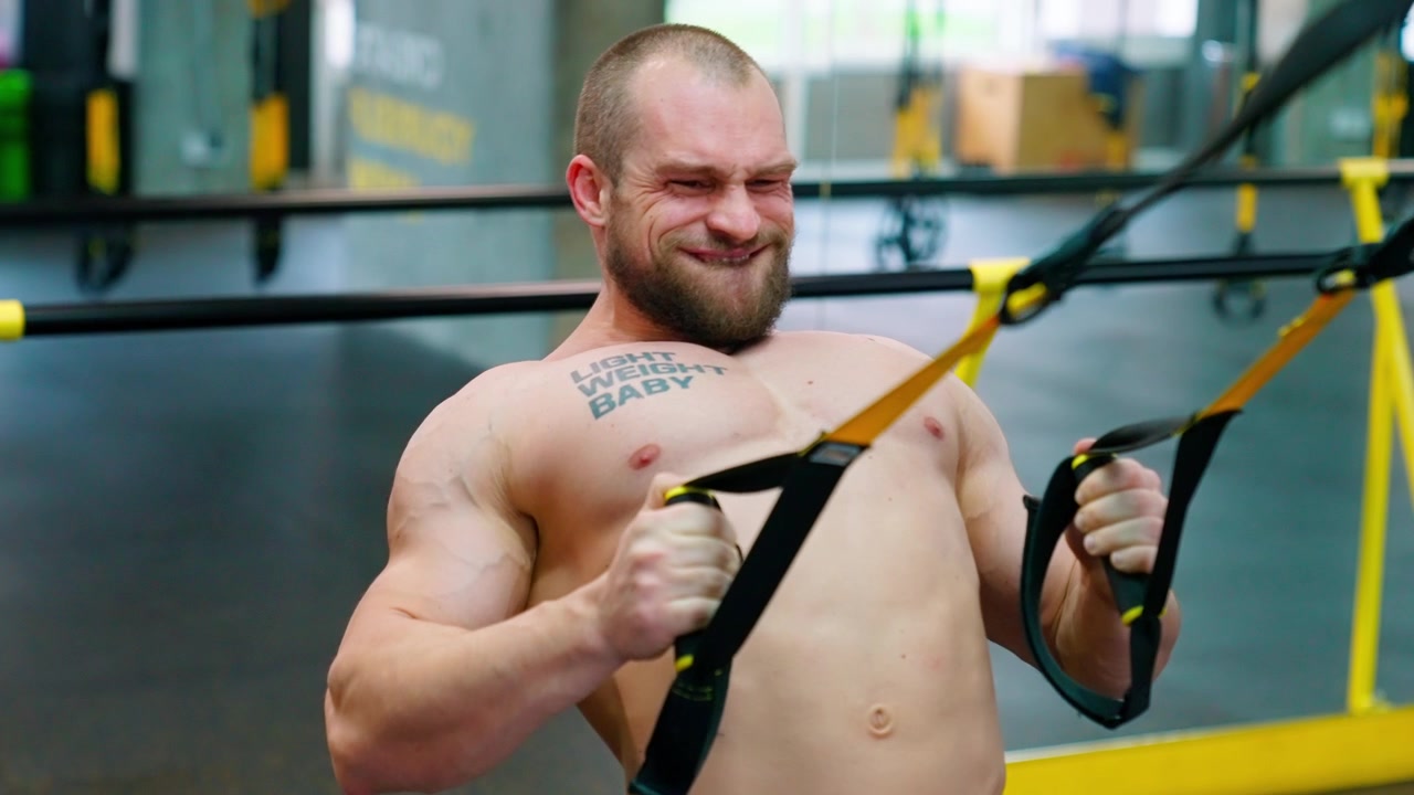 Uomo muscoloso che si allena con le cinghie di sospensione TRX in palestra