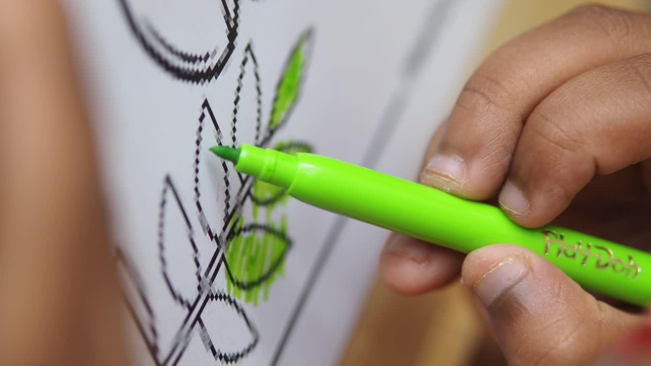 Close-up of a hand coloring a leaf drawing with a green marker
