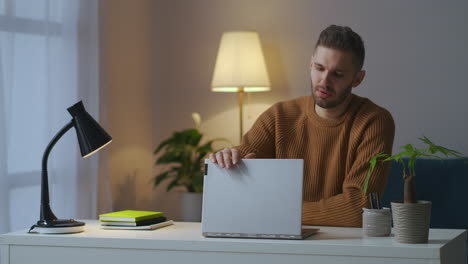 Müder-Männlicher-Student-Schließt-Nach-Einer-Online-Vorlesung-Seinen-Laptop-Und-Sitzt-Abends-Zu-Hause-Und-Berührt-Sein-Gesicht-Mit-Den-Handflächen,-Während-Er-Die-Tischlampe-Ausschaltet