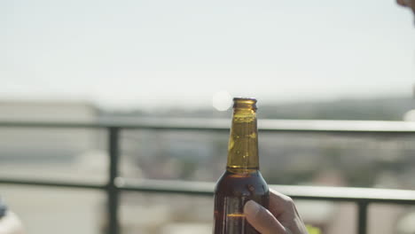 primer plano de dos amigos irreconocibles tintineando botellas de cerveza mientras hacen una fiesta en la azotea