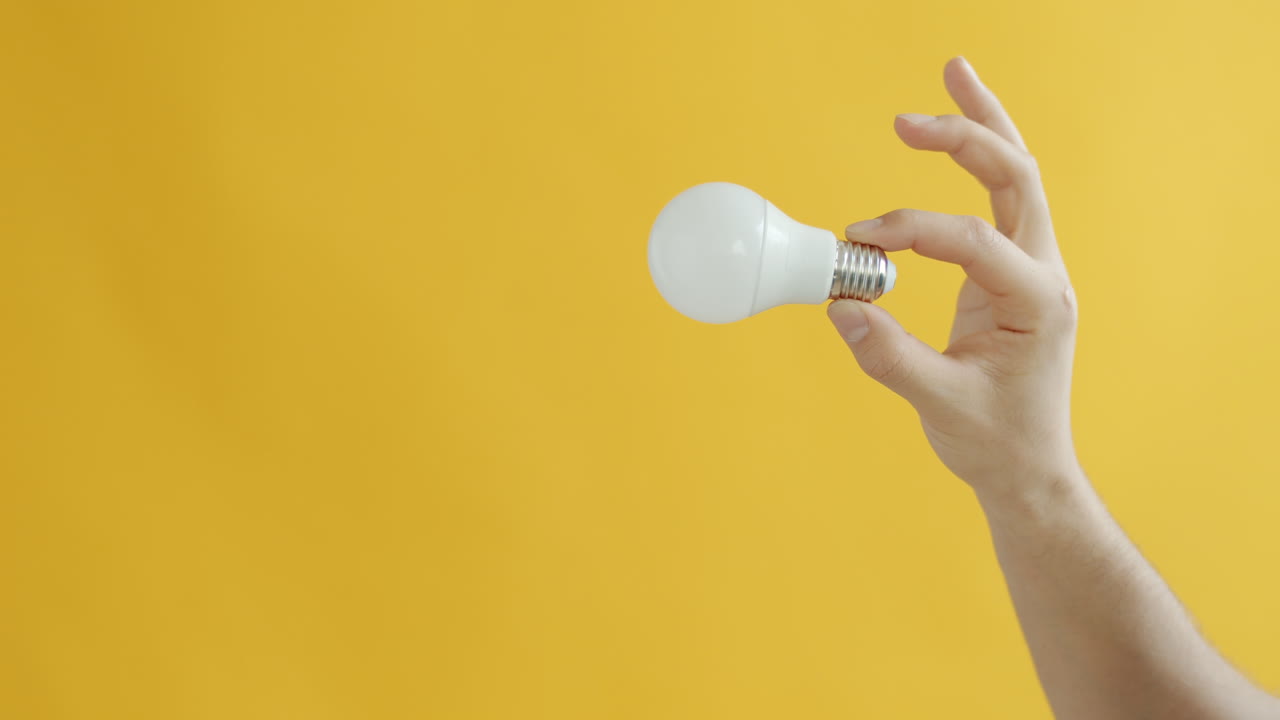 Hand Holding a Light Bulb on a Yellow Background