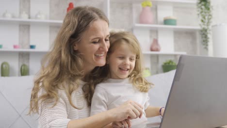 madre y hija pequeña miran la computadora portátil en casa.