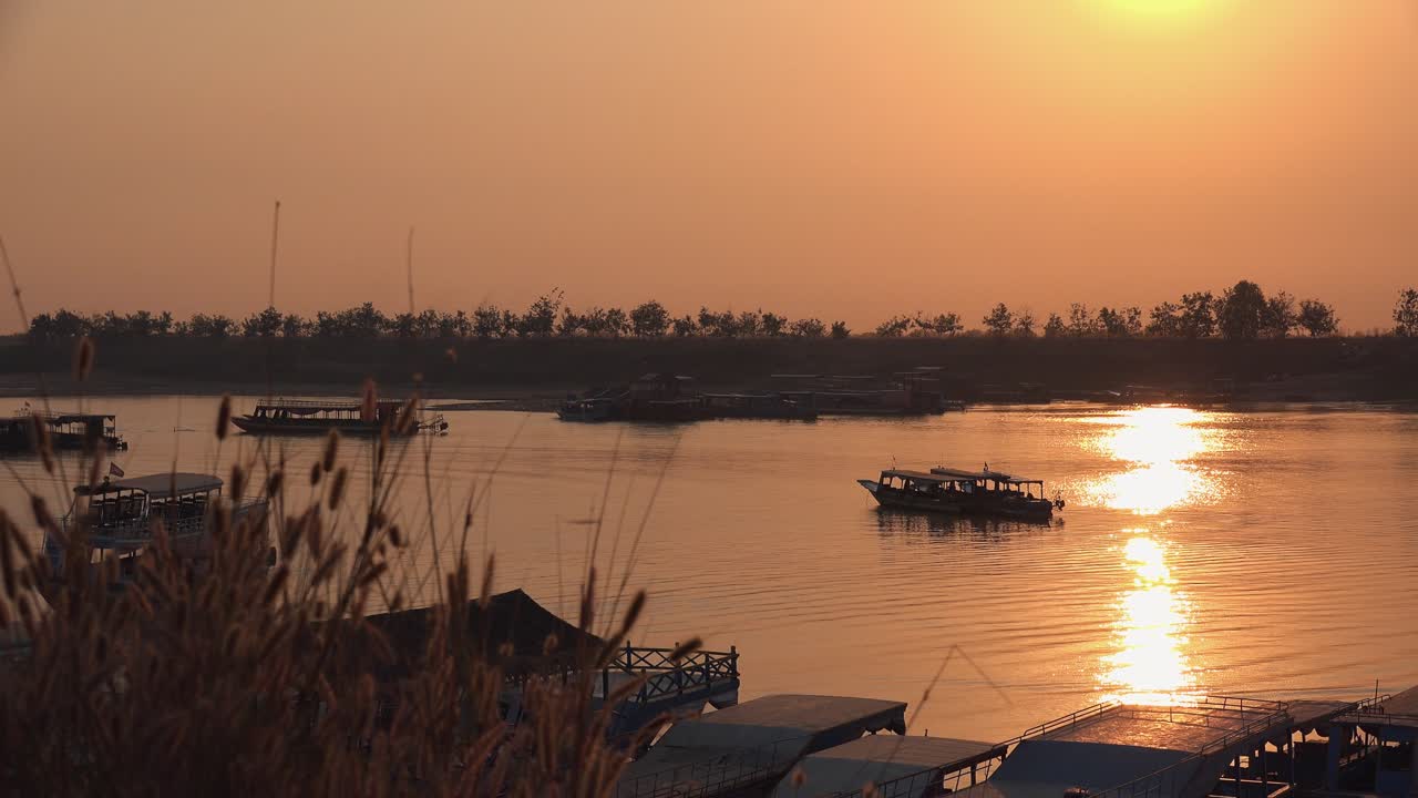 Wide Exterior Shot of Boats Floating In a Lake as the Sun Sets in Golden Hour With an Orange Glow and the Water Moving With Trees on the Horizon