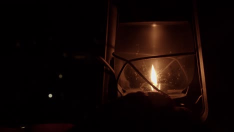 dim night scene: hand adjusts flame smaller in kerosene oil lantern