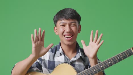 close up of asian teenager with guitar showing gesture hands palm, saying wow, and smiling on green screen background