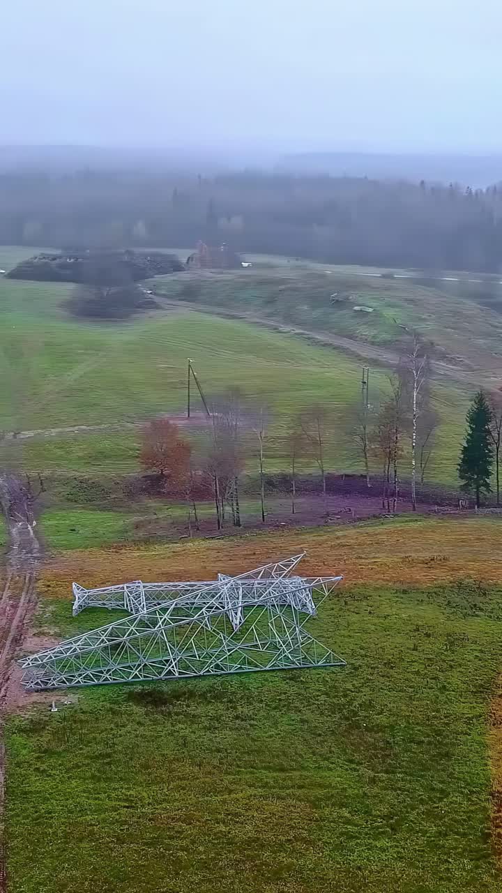 Drone orbits electric pylon frame laid on ground at foggy field staging location