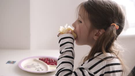 A-little-girl-is-sitting-on-chair-and-eats-thin-pancakes-in-striped-shirt