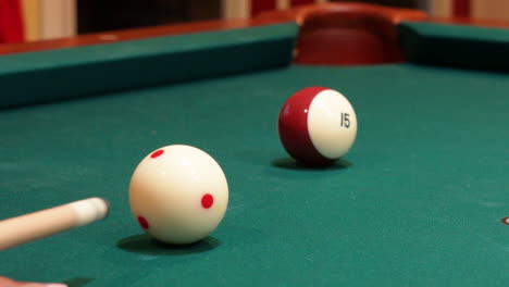 closeup of person playing pool shooting striped brown 15 ball into corner pocket after practice strokes using cue ball with red spots, open bridge hand with wooden cue stick and green felt or cloth