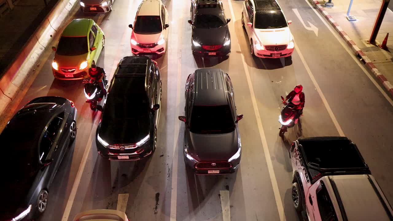 Motorbike rider weaves through congested night traffic under city lights, overhead perspective, urban environment