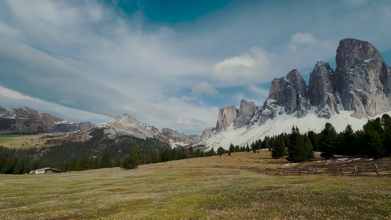 Spektakulære takkede bjergtoppe med sneflekker over grøn eng og træhytte, Sydtyrol Dolomitterne, Italien.