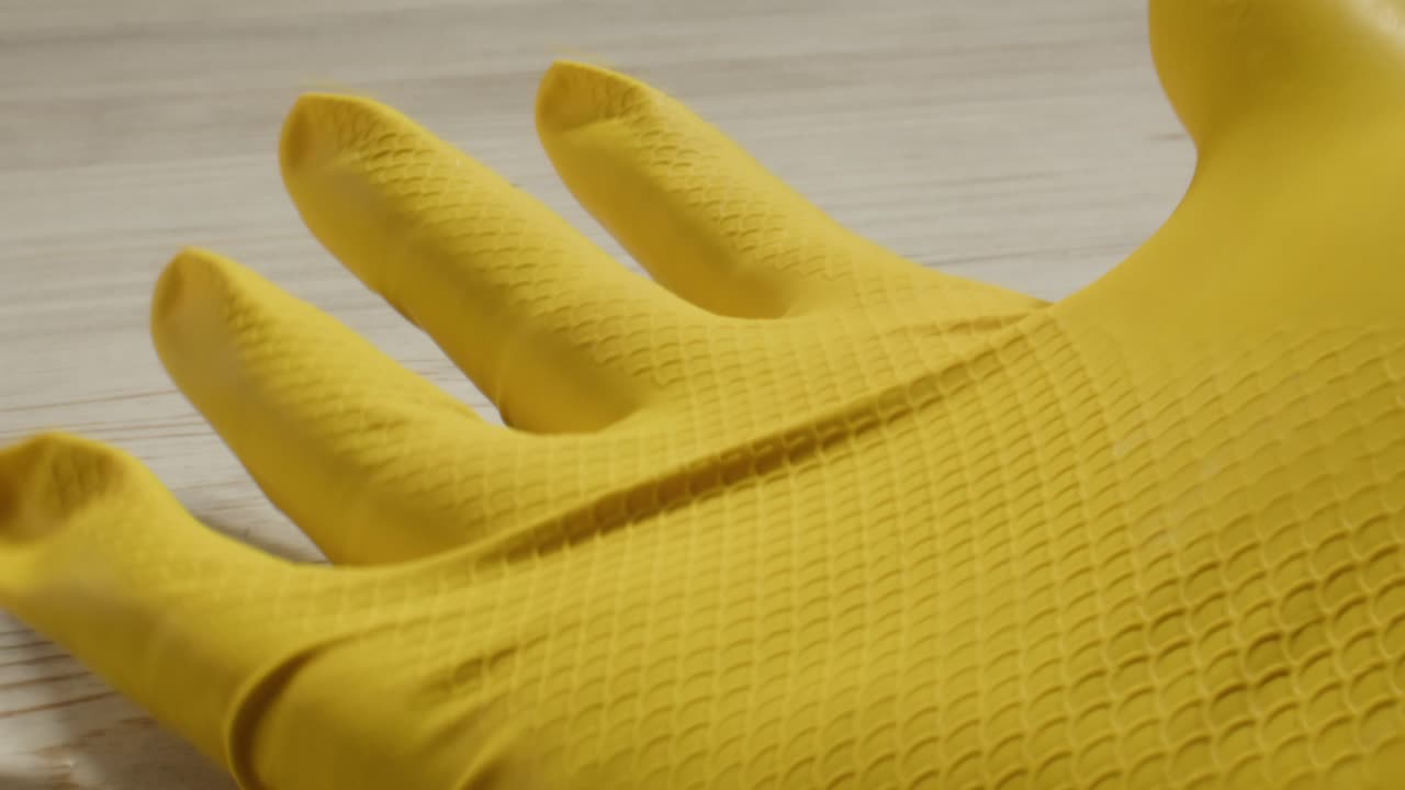 Close-up of Yellow Rubber Glove Flexing on Wooden Surface
