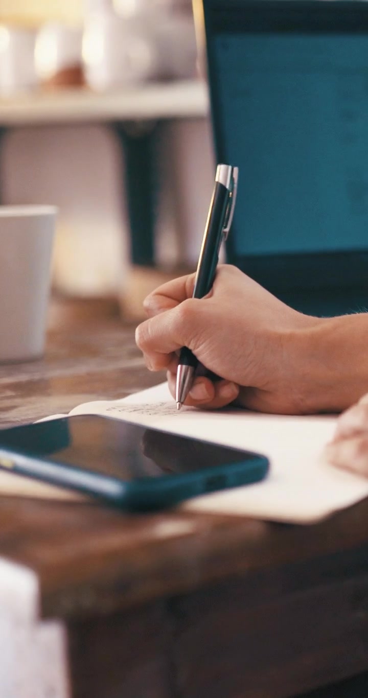 Person Writing in Notebook at Desk with Smartphone