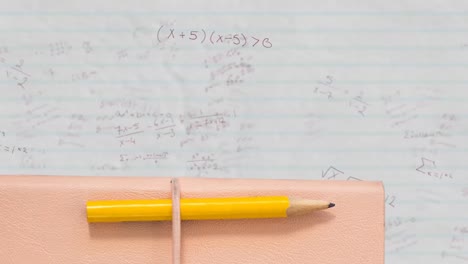 Pencil-and-book-against-mathematical-equations-on-white-lined-paper