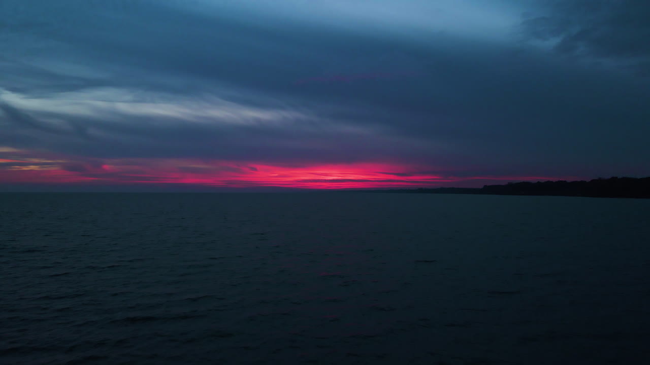 夕暮れ時、穏やかな水面の上、雲の向こうからピンクと赤の最後の輝きが差す。