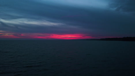 El-Resplandor-Rojo-Rosado-Final-Se-Emite-Detrás-De-Las-Nubes-Sobre-Aguas-Tranquilas-Al-Atardecer