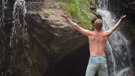 Man-tourist-raises-up-hands-enjoying-waterfall-at-highland